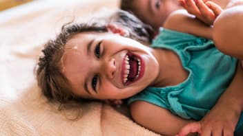 Ein junges Mädchen liegt auf dem Bett und lacht.