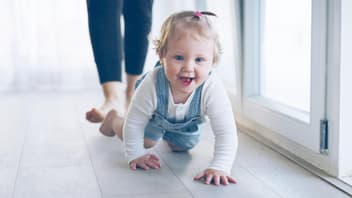 Kleines Mädchen krabbelt grinsend über den Fußboden.