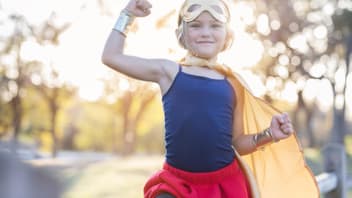 Kleines blondes Mädchen im Superhelden-Kostüm zeigt, wie stark sie ist.