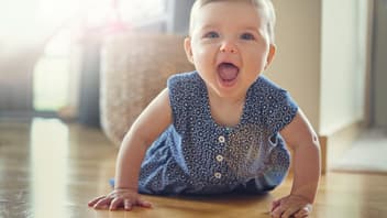 Baby-Mädchen robbt auf dem Boden und lacht mit offenen Mund.