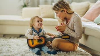 Eine Mama applaudiert ihrem kleinen Sohn, weil er Gitarre spielt