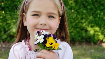 Kleines Mädchen zeigt eine der zwei Februar-Geburtsblumen in die Kamera: das Veilchen. 
