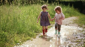 Zwei Kinder laufen durch eine Pfütze.