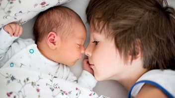 Großer Bruder liegt neben Baby im Bett.