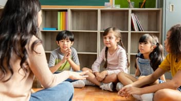 Lehrerin sitzt mit Grundschulkindern auf dem Boden.