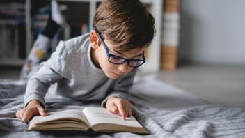 Junge, der auf dem Boden liegt und ein Buch liest.