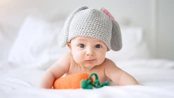 Baby mit Hasenmütze vor Spielzeug-Möhre.