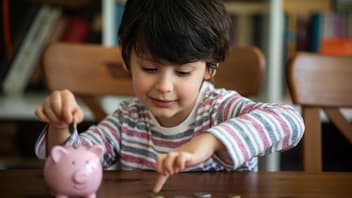 Junge steckt Geld in sein Sparschwein.