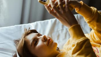 Frau im Bett am Handy mit Kopfhörern.