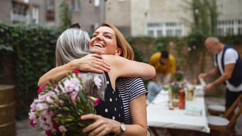Erwachsene Frau umarmt ihre Mutter mit Blumen.