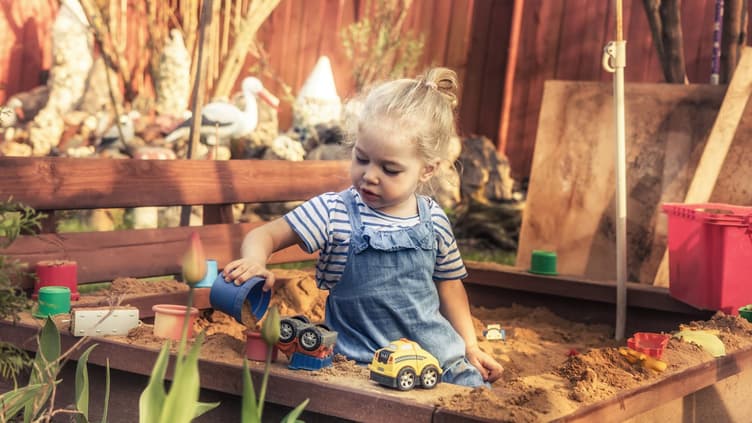Kleines Mädchen spielt mit Autos in der Sandkiste