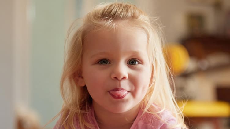 Ein kleines blondes Mädchen streckt die Zunge heraus.