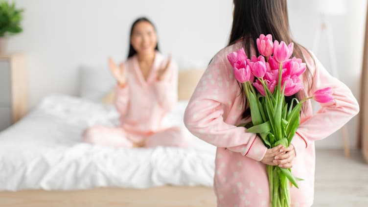 Mädchen versteckt Blumen für ihre Mutter hinter ihrem Rücken