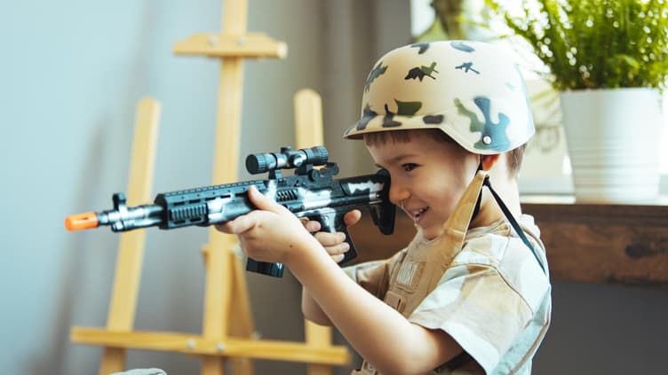 Kleiner Junge mit Tarn-Helm und Spielzeugwaffe