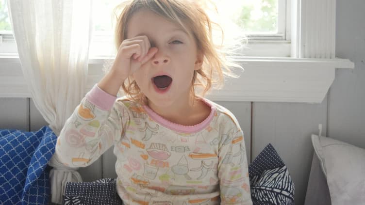 Blondes Mädchen reibt sich am Morgen die Augen und gähnt