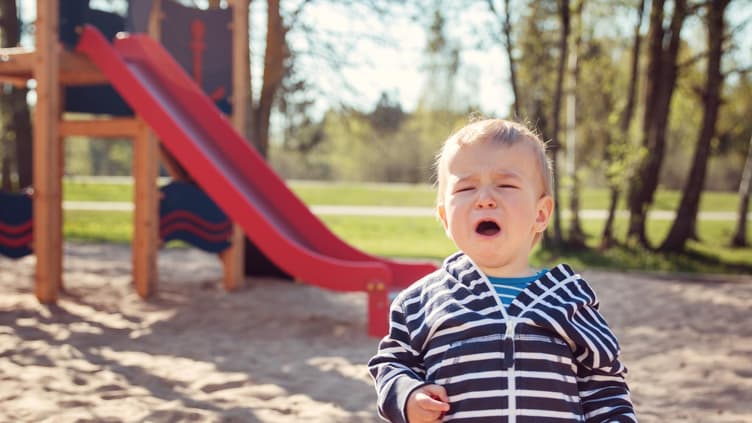 Kleiner Junge sitzt weinend vor einer Rutsche im Sand