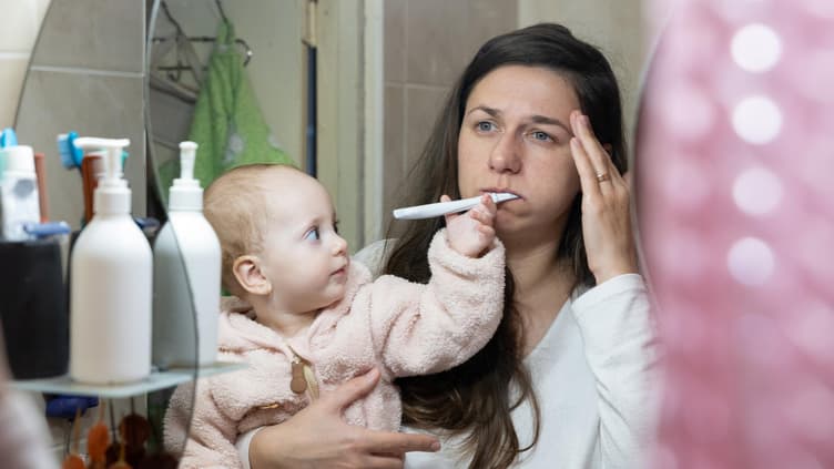 Eine müde Mama und ihr Baby im Badezimmer. 