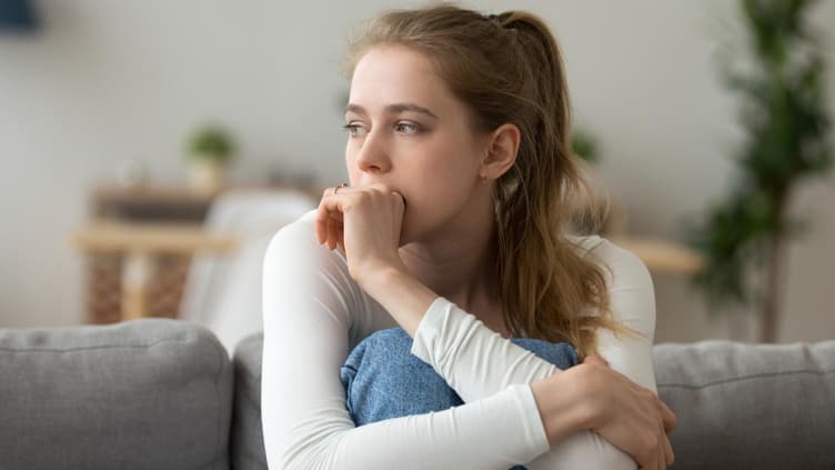 Junge Frau sitzt traurig und nachdenklich zu Hause
