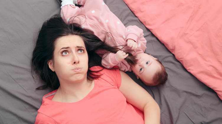 Mama liegt neben Baby auf dem Bett.