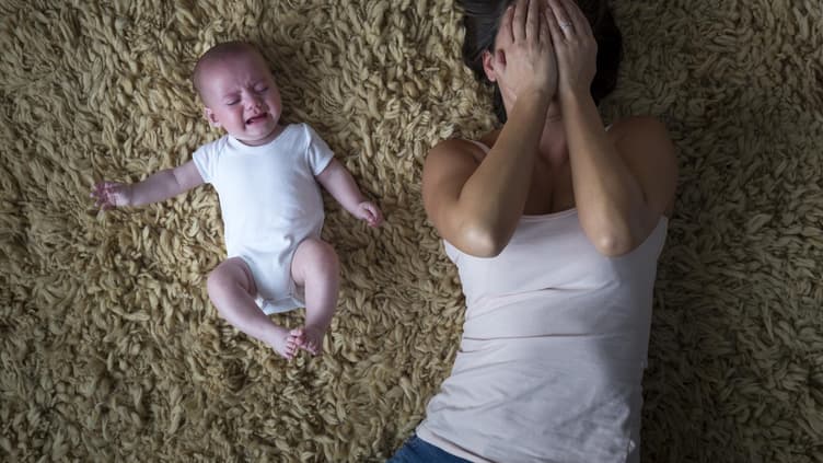 Mutter liegt weinend neben ihrem Baby auf dem Boden 