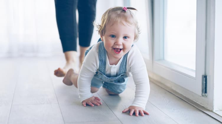 Kleines Mädchen krabbelt grinsend über den Fußboden.