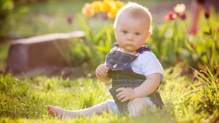 Ein kleiner Junge sitzt auf dem Gras und staunt.