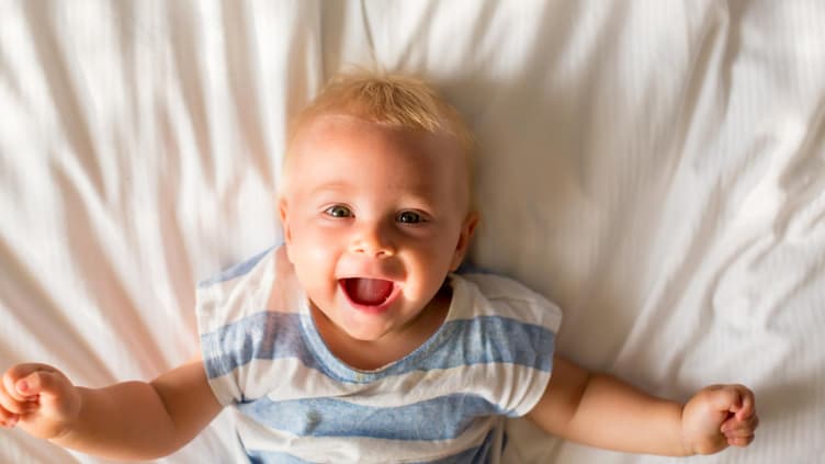 Baby-Junge liegt auf dem Bett und lacht.