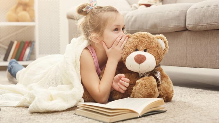 Kleines Mädchen flüstert ihrem Teddy ein Geheimnis ins Ohr.