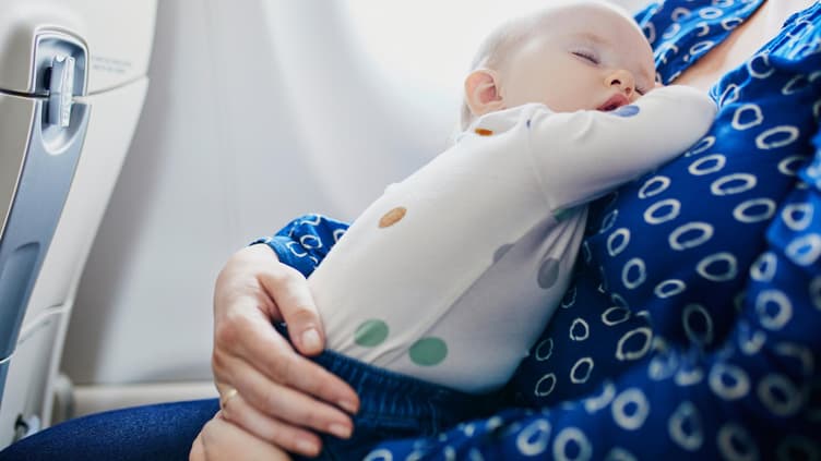 Ein kleines Baby schläft im Flugzeug auf dem Schoß seiner Mutter. 