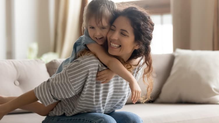 Mutter trägt ihr Kind auf dem Sofa sitzend huckepack.