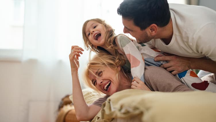Eltern und Kind liegen im Familienbett und lachen.