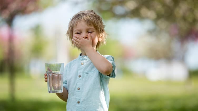 Blonder Junge trinkt Wasser im Park.