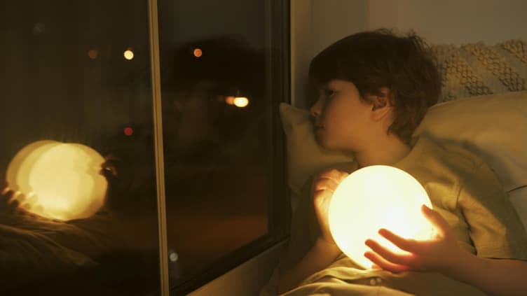 Ein Kind, das beim Einschlafen traurig aus dem Fenster guckt