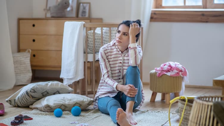 Erschöpfte Frau sitzt auf dem Boden im Kinderzimmer.