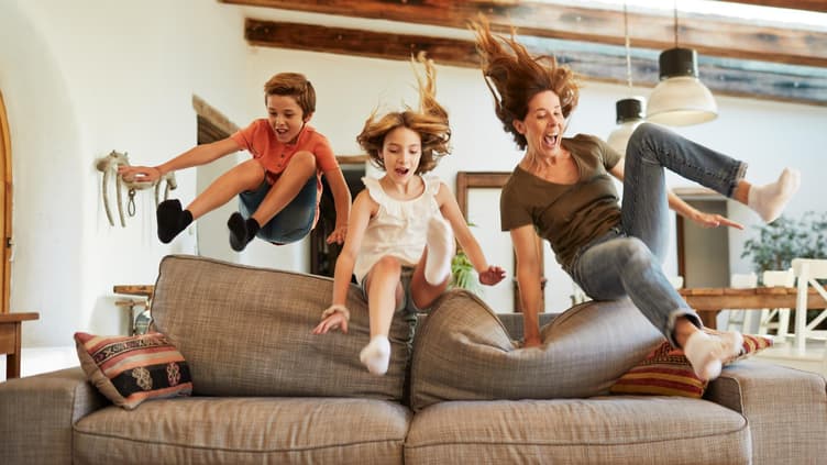 Mutter und zwei Kinder springen zusammen aufs Sofa