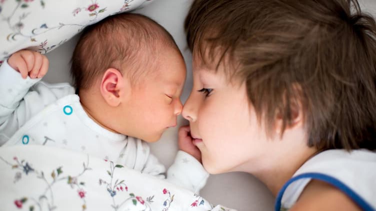 Großer Bruder liegt neben Baby im Bett.