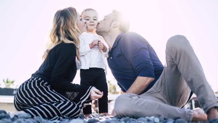 Eltern umringen ihr Kind und küssen es.