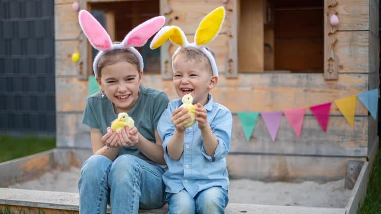 Zwei Kinder mit Osterhasenohren und einem Küken in der Hand