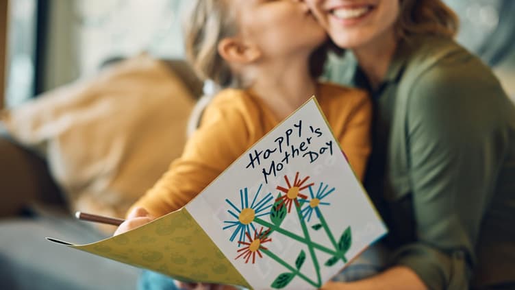 Kind küsst Mutter und schenkt ihr eine Karte zum Muttertag.