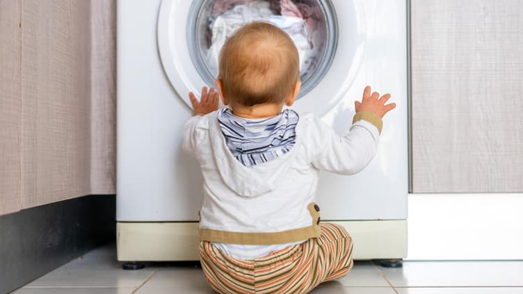 Baby sitzt vor der Waschmaschine und schaut hinein.