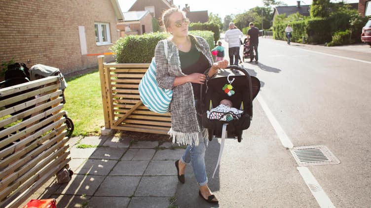 Eine Mutter trägt ihr Baby im Maxi Cosi über die Straße