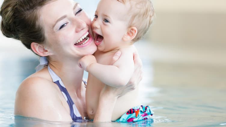 Ein Baby in Schwimmwindeln plantscht mit seiner Mutter im Schwimmbad. 