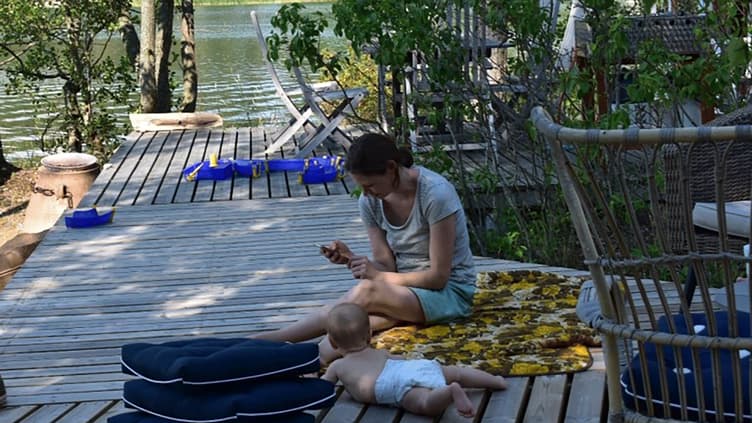 Mutter mit Baby am Wasser mit Handy in der Hand.