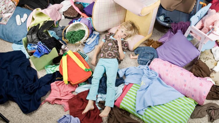 Kind liegt in chaotischem Kinderzimmer auf dem Boden.