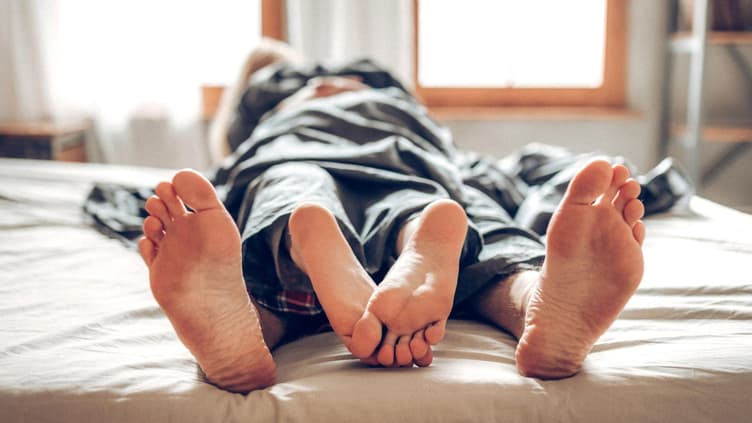 Paar liegt unter dem Laken aufeinander, die Füße schauen heraus.