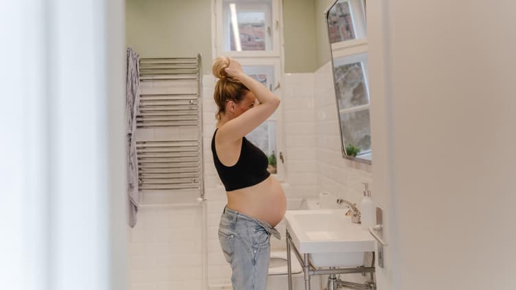 Eine schwangere Frau färbt sich vor dem Spiegel die Haare. 