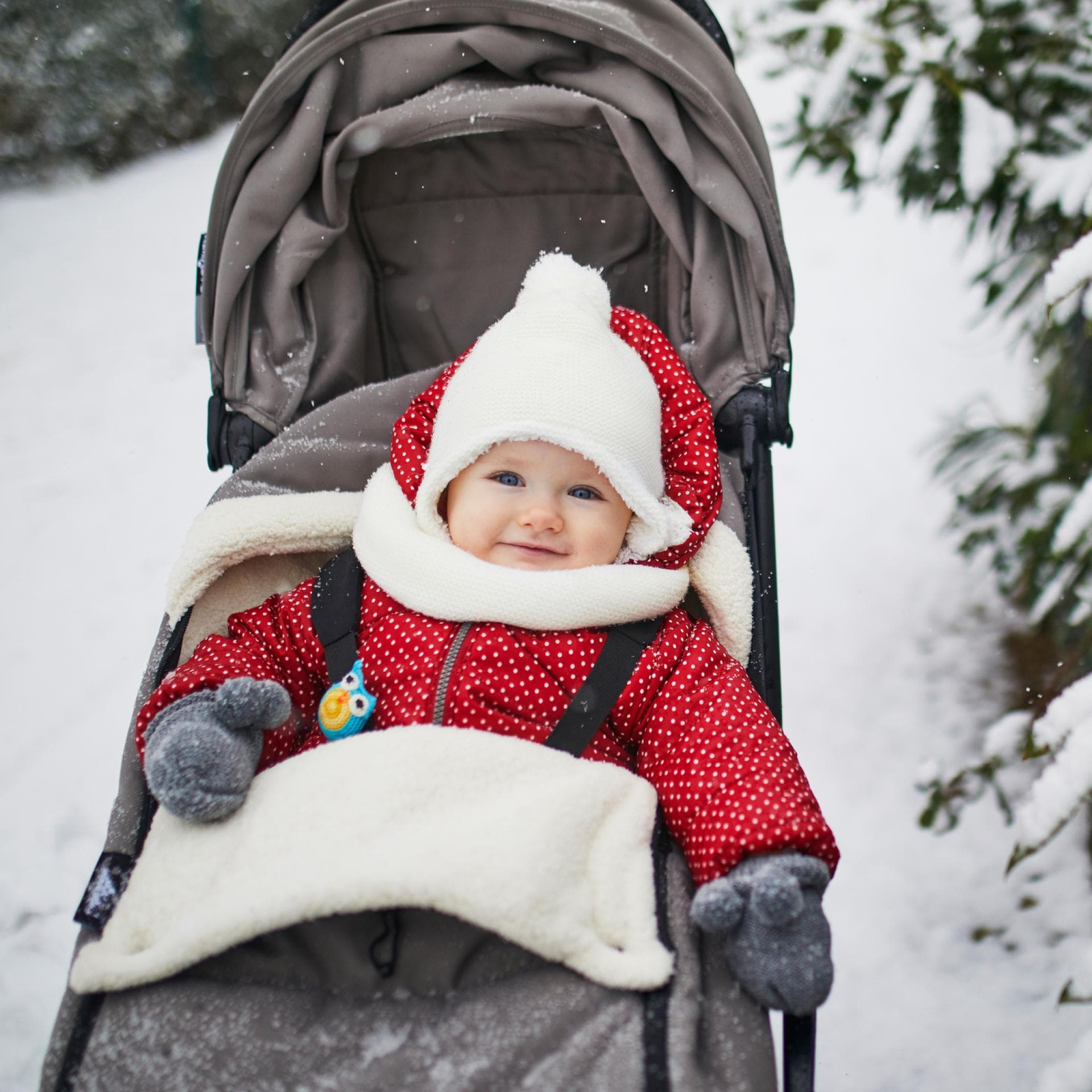 Ein kleines Mädchen sitzt dick eingepackt im Kinderwagen, der im Schnee steht.