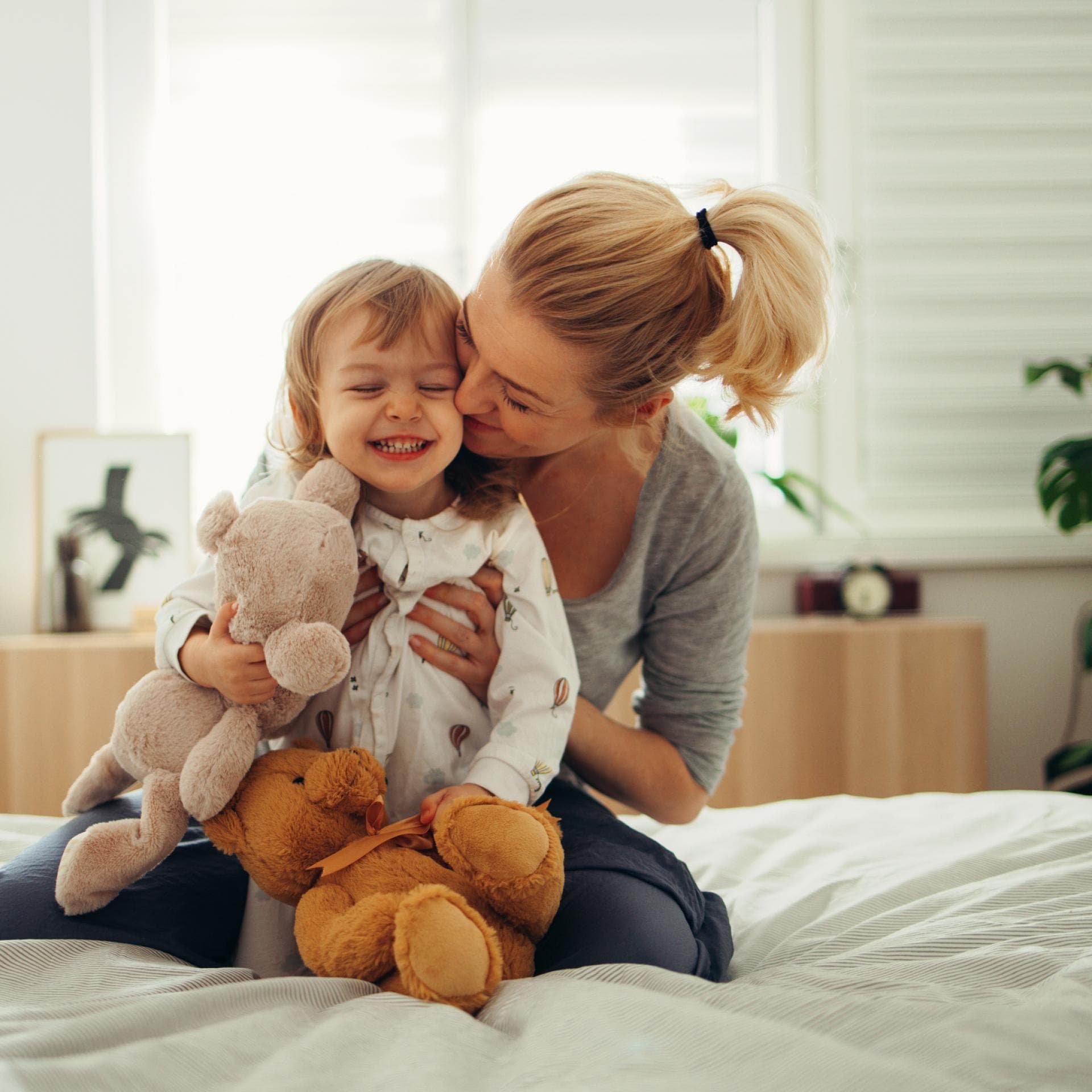 Mama umarmt Mädchen mit Kuscheltieren