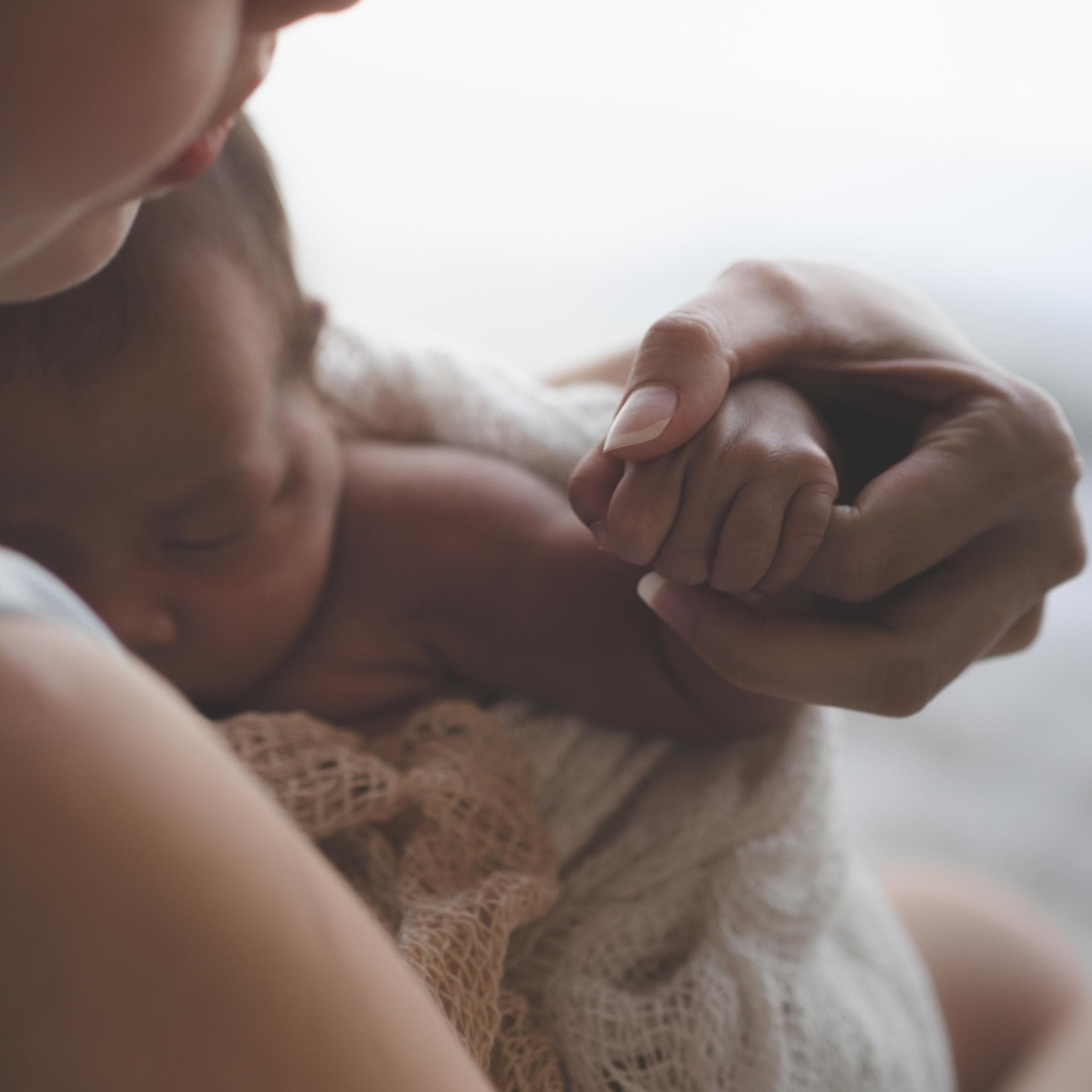 Mutter hält ihr Neugeborenes eingewickelt im Arm
