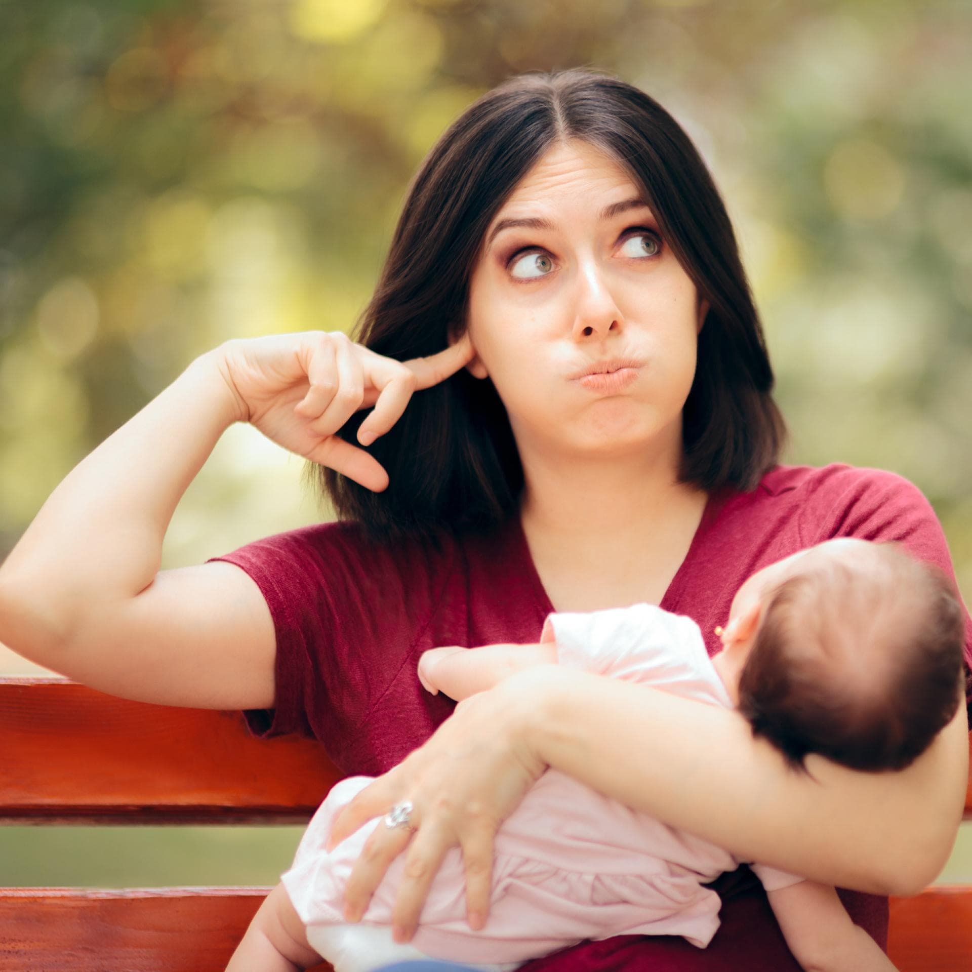 Mutter mit Baby im Arm hält sich die Ohren zu.